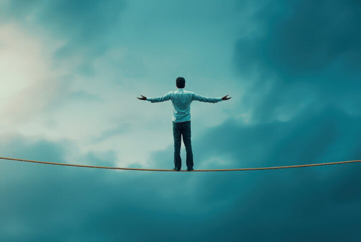 man balancing on high wire with arms open and back to camera